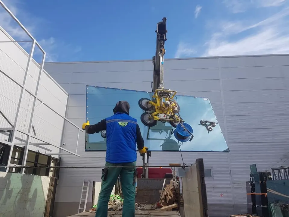 Montator MAST poziționând un geam mare cu ventuza pe structura unui perete cortină